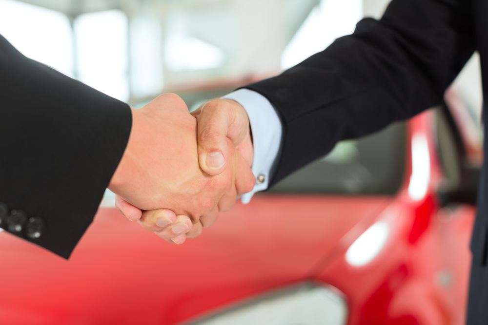 Image Of Two Men's In Black Suits Hand Shaking with the Red Car At the Back