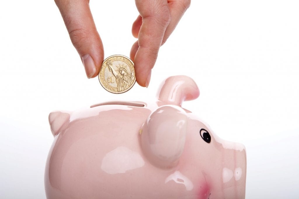 A hand placing a coin into a pink piggy bank.
