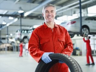 Portrait of smiling mechanic holding tire in auto repair shop